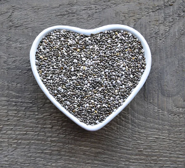 Beyaz kalp içinde Chia tohum eski ahşap arka plan üzerinde kase şeklinde. Ada çayı hispanica tohumları. Sağlıklı gıda veya superfood kavramı.