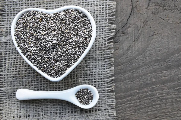 Beyaz kalp içinde Chia tohum eski ahşap arka plan üzerinde kase şeklinde. Ada çayı hispanica tohumları. Sağlıklı gıda veya superfood kavramı.