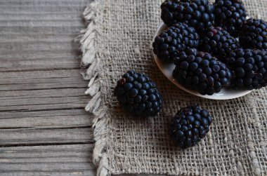 Çuval bezi eski ahşap arka plan üzerinde beyaz bir tabağa olgun böğürtlen. BlackBerry.