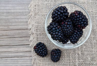 Eski ahşap arka plan üzerine çuval bezi kumaş üzerinde bir cam kasede olgun böğürtlen. Blackberry.Healthy yiyecek ya da diyet kavramı.
