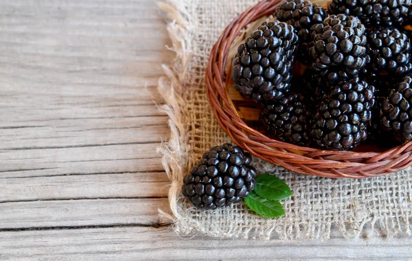 Ripe blackberries in a basket on burlap cloth on old wooden background.Blackberry.Healthy food or diet concept.