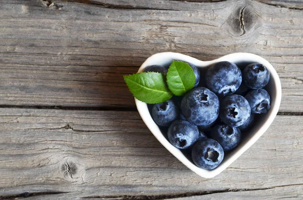 Taze organik yaban mersini bir beyaz kalp rustik ahşap masa üzerine çuval bezi kumaş kase şeklinde. Blueberry.Bilberries.Healthy yeme, vegan gıda, diyet ve beslenme kavramı.
