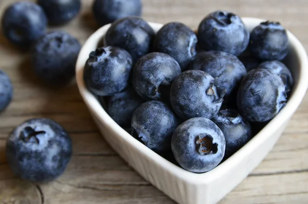 Verse biologische bosbessen in een wit hart vormige kom op een jute doek op rustieke houten tafel. Blueberry.Bilberries.Healthy eten, veganistische voeding, dieet en voeding concept. — Stockfoto