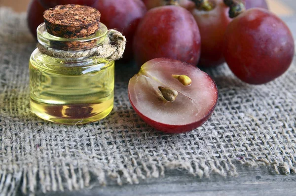 Grape seed oil in a glass jar and fresh grapes on old wooden table.Bottle of organic grape seed oil for spa and bodycare and grape berries.Spa,Bio,Eco products concept.Selective focus.