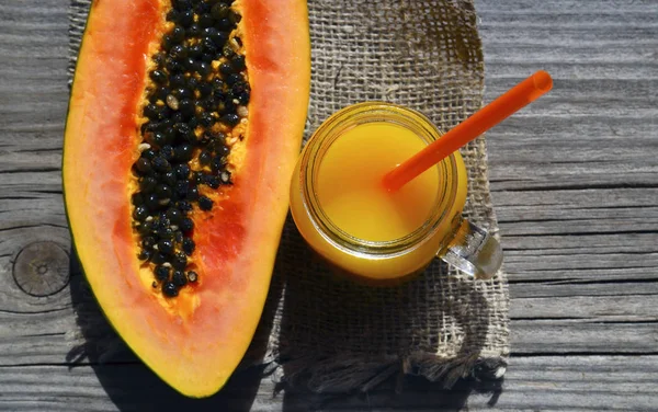 Fresh papaya juice in a glass jar and ripe papaya fruit on old wooden table in summer garden.Healthy drink,diet or vegan food concept.Selective focus.