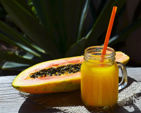 Fresh papaya juice in a glass jar and cut in half ripe papaya fruit on old wooden table in tropical garden.Healthy drink,detox,diet or vegan food concept.Selective focus.