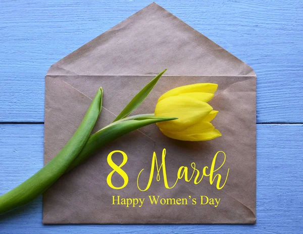 Happy Women\'s Day.Yellow tulip and paper envelope with text on blue wooden background.International Women\'s Day 8th March greeting card.Selective focus.