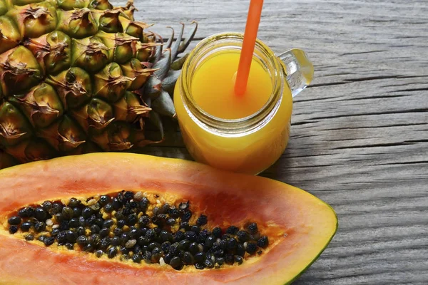 Olgun organik papaya ve ananaslı tropikal meyve ikiye bölünmüş ve eski ahşap arka planda cam bir kavanozda taze meyve suyu. Sağlıklı beslenme, diyet veya vegan gıda kavramı..