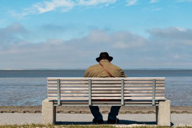 Deniz kenarında bir bankta oturan şapkalı adam