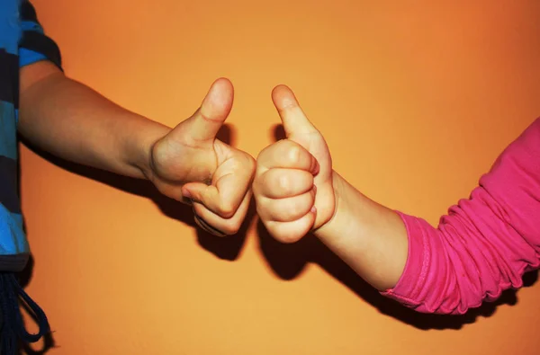 Crianças mostrando dois polegares para cima no fundo laranja — Fotografia de Stock