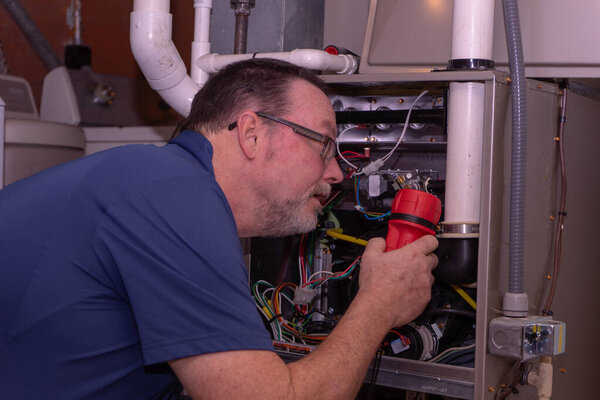 HVAC Technician Inspecting A Gas Furnace Blue Shirt 