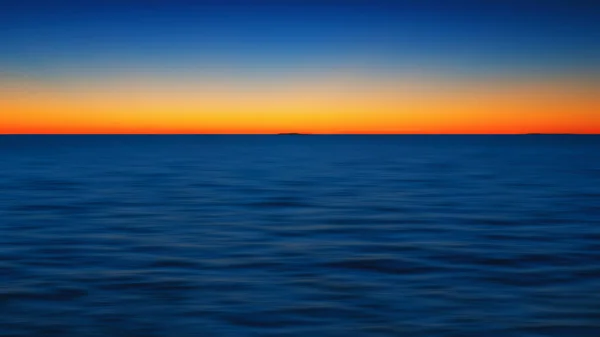 Yellow-orange glow in the dark blue sky above the horizon after sea sunset. Abstract motion blurred seascape background with copy space. Russia, Lake Onega. Color 2020.