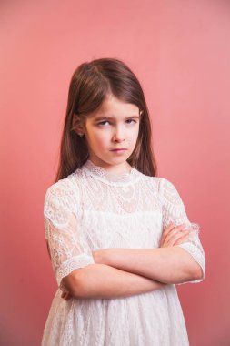 a beautiful girl in a white dress playfully poses on a pink background