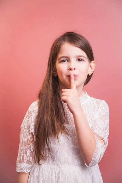 a beautiful girl in a white dress playfully poses on a pink background