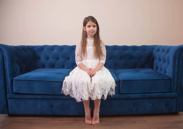 a beautiful girl sits on a blue sofa and looks sad