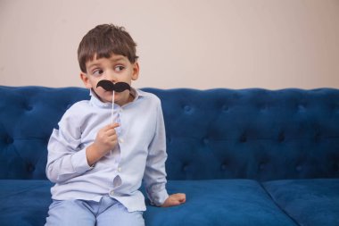 a boy with big eyes plays with a paper toy black mustache