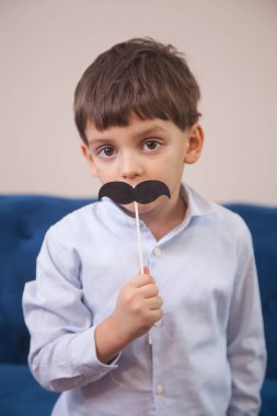 a boy with big eyes plays with a paper toy black mustache