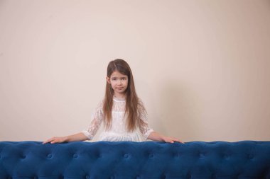 Kız mavi bir kanepede oturuyor, parlak bir odada ve poz veriyor.