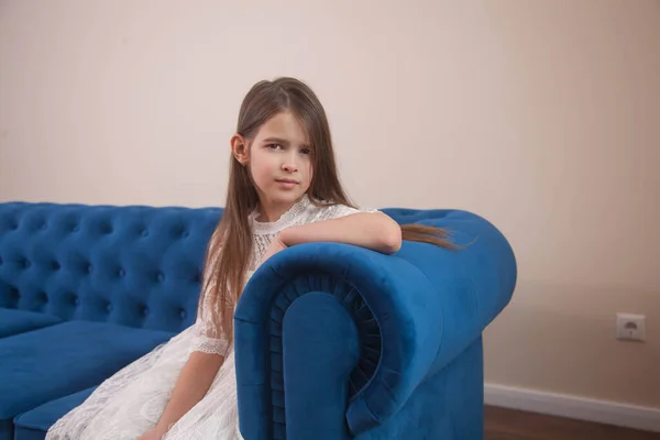 女孩坐在一间明亮房间里的蓝色沙发上 摆着姿势 — 图库照片