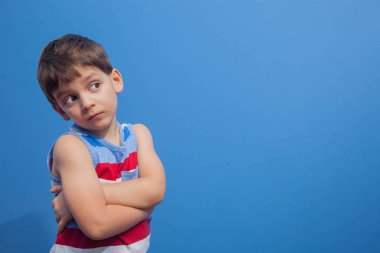 Çizgili tişörtlü genç bir çocuk mavi arka planda model olarak poz veriyor.
