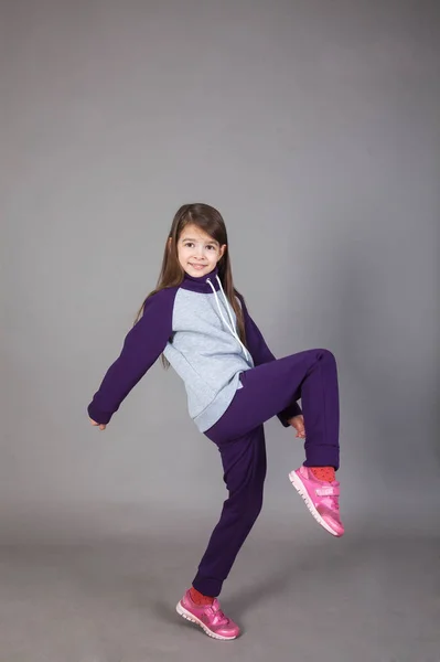 Spor giyimli genç bir kız gri arka planda bunu gösteriyor.