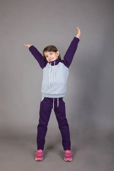 Spor giyimli genç bir kız gri arka planda bunu gösteriyor.