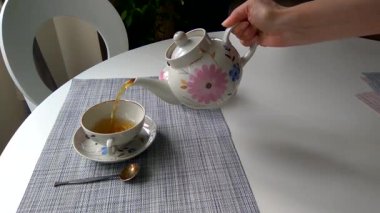 Kız yemek masasındaki fincana çay dolduruyor.