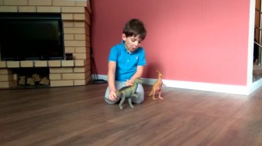 Küçük çocuk evde yerde oyuncak dinozorlarla oynuyor.