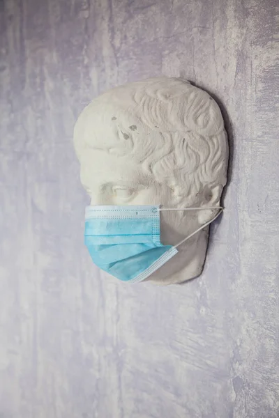 Blue protective medical mask worn on an old Roman statue