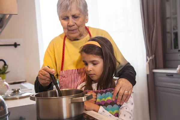 Grandma and granddaughter cook food in a pot on the stove in the kitchen