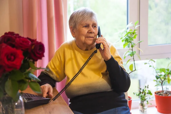 Büyükannem telefonda, rahat bir odada çiçekli bir sandalyede oturuyor.