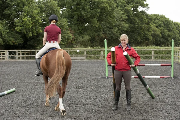 Flicka som rider en ponny och instruktör bära staket stolpar — Stockfoto