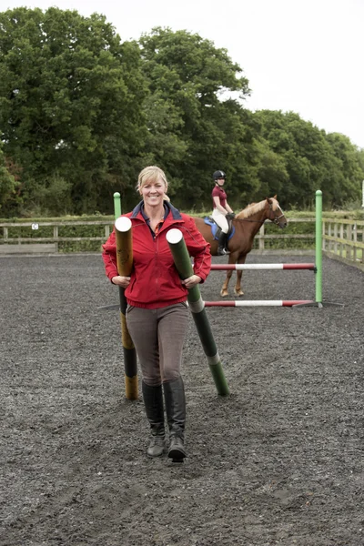 Flicka som rider en ponny och instruktör bära staket stolpar — Stockfoto