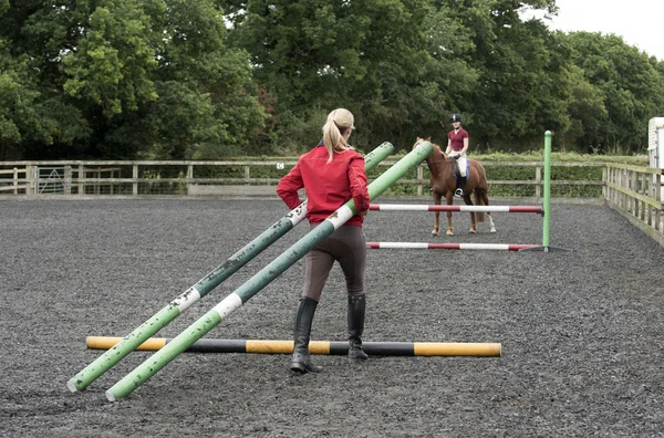 Flicka som rider en ponny och instruktör bära staket stolpar — Stockfoto