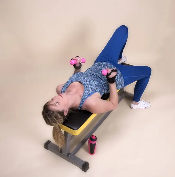Woman laying on a fitness bench working out with weights — Stock Photo, Image