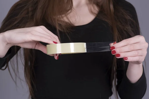 Mujer con un rollo de cinta adhesiva arrancando una longitud del rollo — Foto de Stock