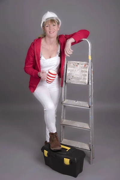 Female worker wearing dungarees drinking from a mug — Stock Photo, Image