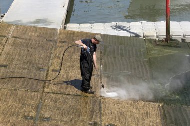 Adam bir waterjet kullanarak bir liman kızak alglerden temizlik. İngiltere