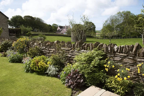 Uma parede de pedra seca e plantas dividem jardins em um jardim inglês Reino Unido — Fotografia de Stock