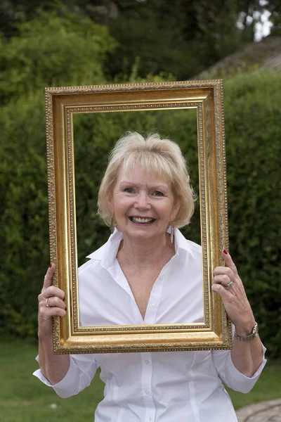 Elderly blond woman holding a picture frame — Stock Photo, Image