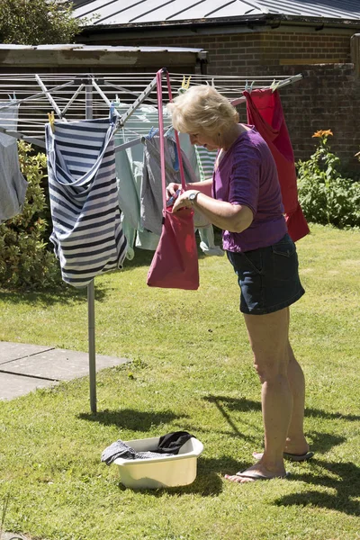 Äldre kvinna och peg väska som hon hänger ut tvätt — Stockfoto