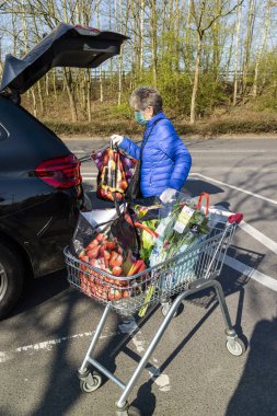 Southampton, İngiltere, İngiltere. Mart 2020. Coronavirus salgını sırasında korunmak için maske ve lastik eldiven takan yaşlı bir kadın market alışverişini arabaya yüklüyor..