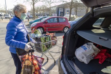 Southampton, İngiltere, İngiltere. Mart 2020. Coronavirus salgını sırasında korunmak için maske ve lastik eldiven takan yaşlı bir kadın market alışverişini arabaya yüklüyor..