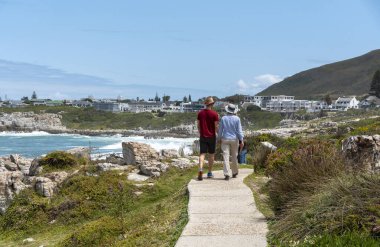 Hermanus, Batı Burnu, Güney Afrika. 2019. Hermanus 'un sahil şeridindeki biyolojik çeşitlilikteki turistler, Güney Afrika' nın bahçe rotasında popüler bir sahil beldesi olan Hermanus 'ta yürürler.