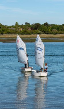Lymington, Hampshire, İngiltere, İngiltere. Mayıs 2020. Genç bir oğlan ve kız New Forest, Hampshire, İngiltere 'deki Lymington Nehri' nde Optomist yelkenli kullanmayı öğreniyorlar..