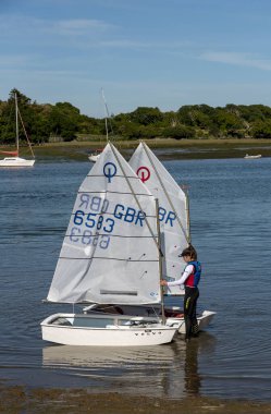 Lymington, Hampshire, İngiltere, İngiltere. Mayıs 2020. Genç bir oğlan ve kız, İngiltere 'nin Hampshire şehrindeki New Forest, Hampshire' daki Lymington Nehri 'nde Optomist yelkenli kullanmayı öğreniyorlar. Karaya çıkmadan önce iki tekne tutan genç kız..