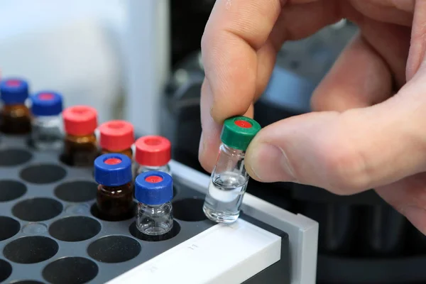 Las personas sostienen a mano un conjunto de frascos de tubo de ensayo para su análisis en el cromatógrafo líquido de gas. Asistente de laboratorio insertando botella de vidrio de laboratorio en un vial de cromatógrafo — Foto de Stock