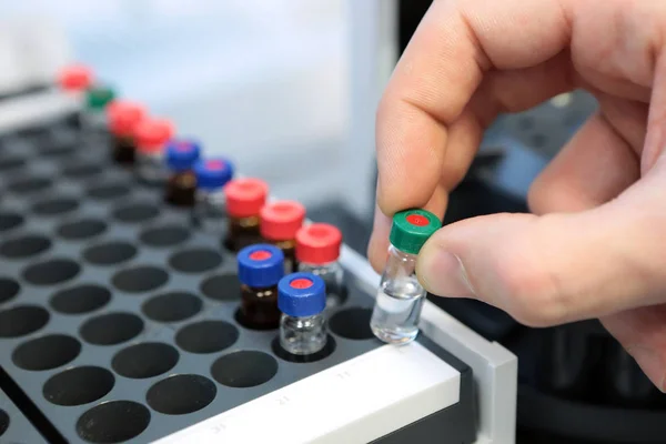 Las personas sostienen a mano un conjunto de frascos de tubo de ensayo para su análisis en el cromatógrafo líquido de gas. Asistente de laboratorio insertando botella de vidrio de laboratorio en un vial de cromatógrafo —  Fotos de Stock