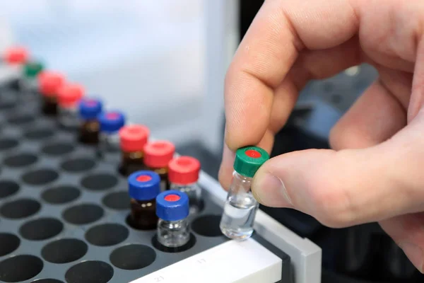 Las personas sostienen a mano un conjunto de frascos de tubo de ensayo para su análisis en el cromatógrafo líquido de gas. Asistente de laboratorio insertando botella de vidrio de laboratorio en un vial de cromatógrafo —  Fotos de Stock