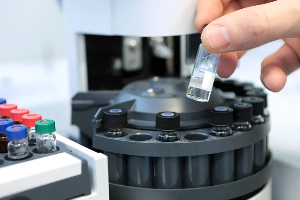 Las personas sostienen a mano un conjunto de frascos de tubo de ensayo para su análisis en el cromatógrafo líquido de gas. Asistente de laboratorio insertando botella de vidrio de laboratorio en un vial de cromatógrafo — Foto de Stock